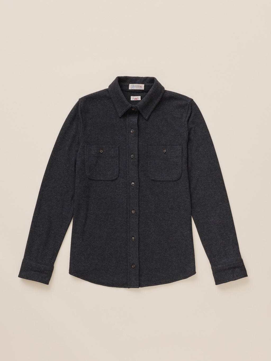 A dark charcoal gray long-sleeve button-up shirt with two buttoned chest pockets, laid flat against a light beige background.