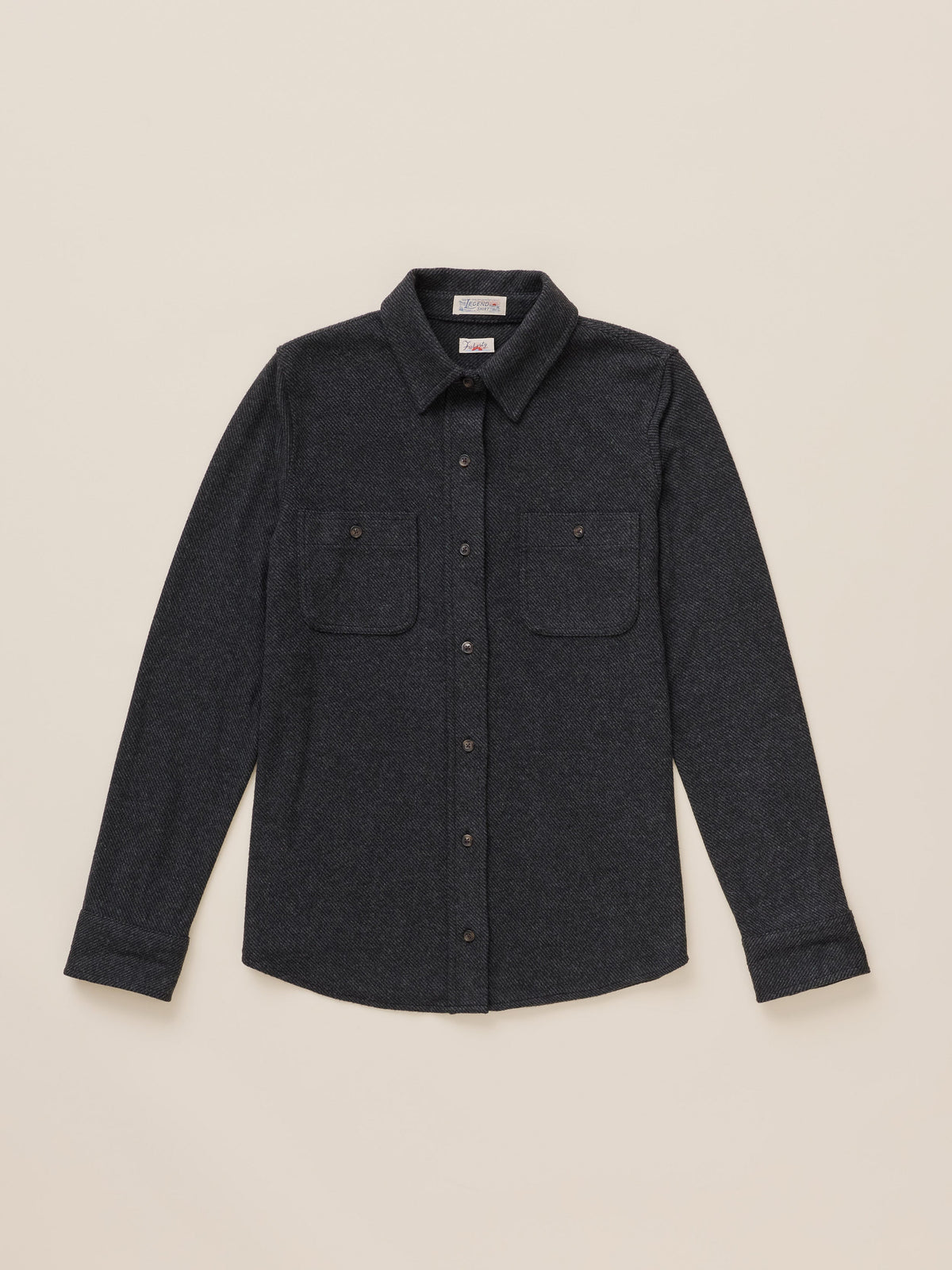 A dark charcoal gray long-sleeve button-up shirt with two buttoned chest pockets, laid flat against a light beige background.