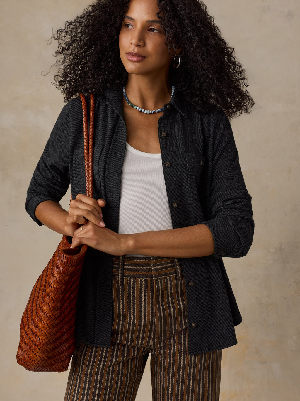 Woman wearing a black sweater shirt with brown striped pants against a beige background