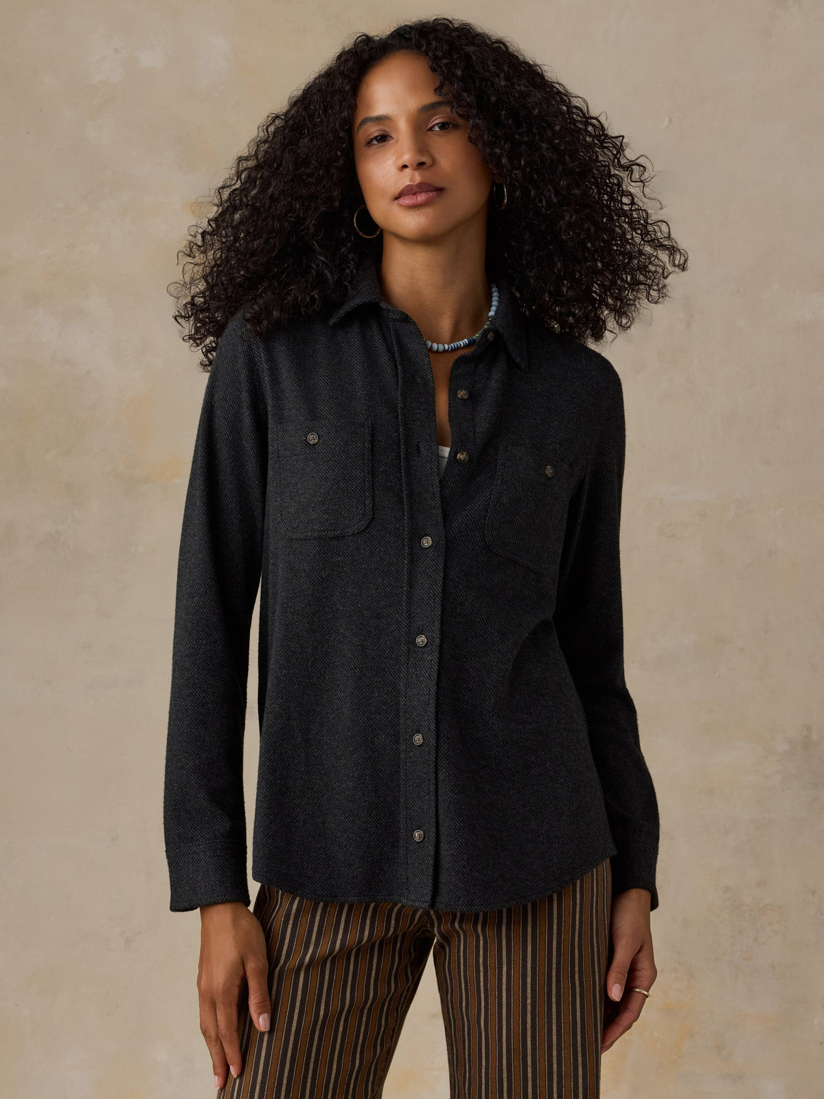 Woman wearing a black sweater shirt with brown striped pants against a beige background