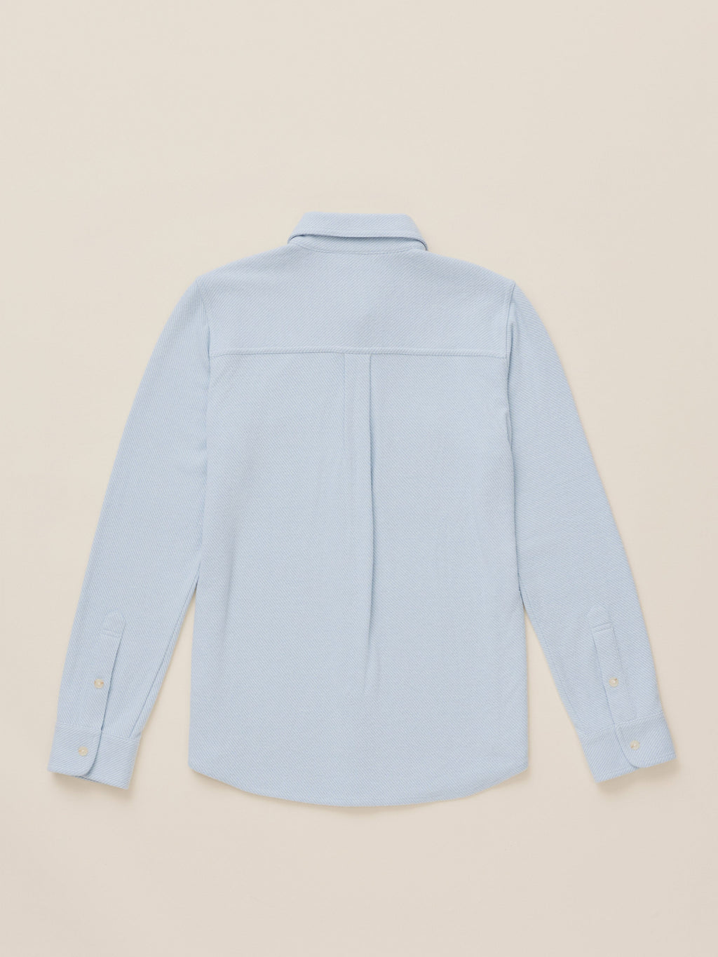 A light blue long-sleeve button-up shirt shown from the back, laid flat against a solid beige background.