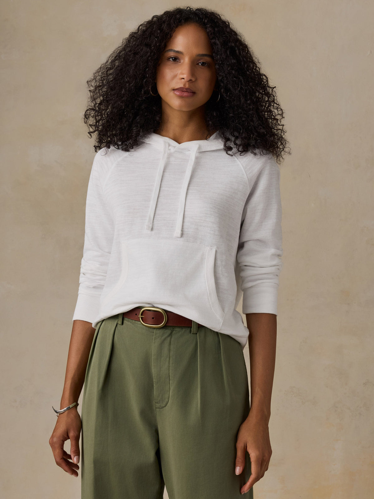 Woman wearing a white hoodie and olive green pants against a beige background