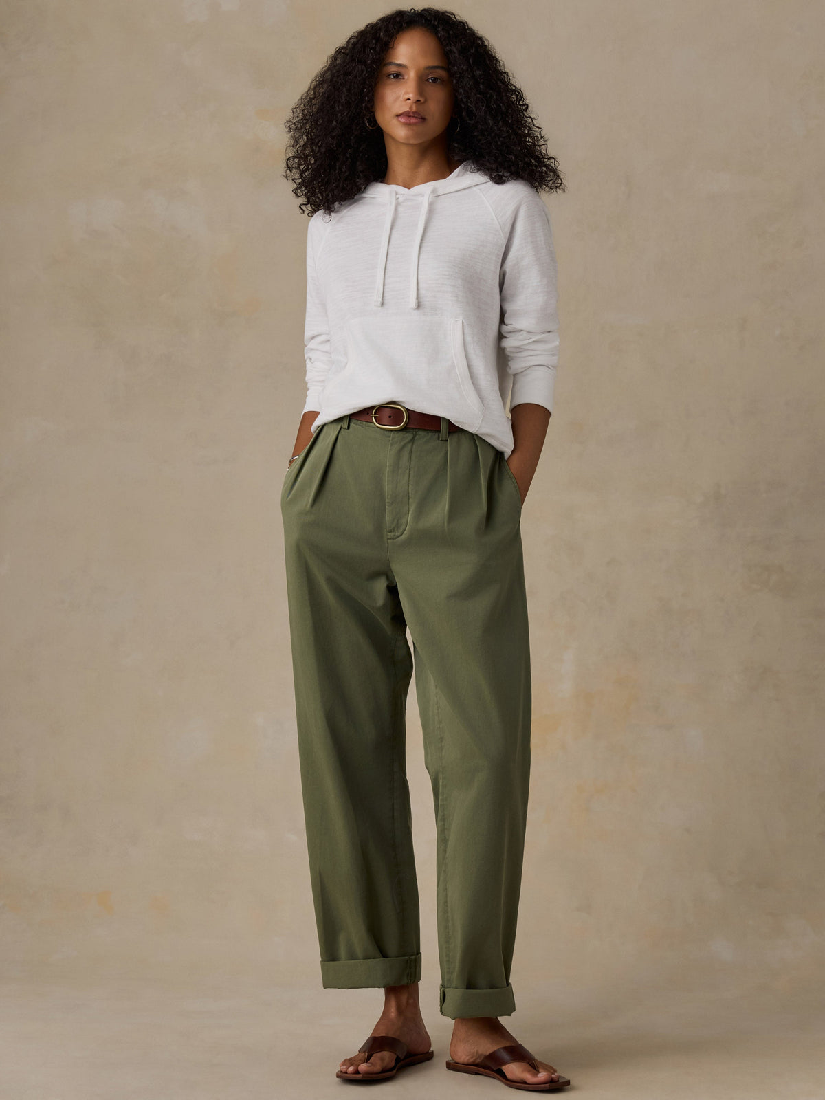 Woman wearing a white hoodie and olive green pants against a beige background