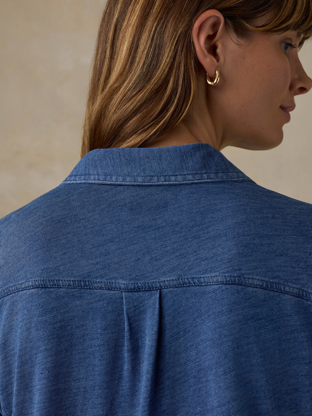 Woman wearing a blue button down shirt against a beige background