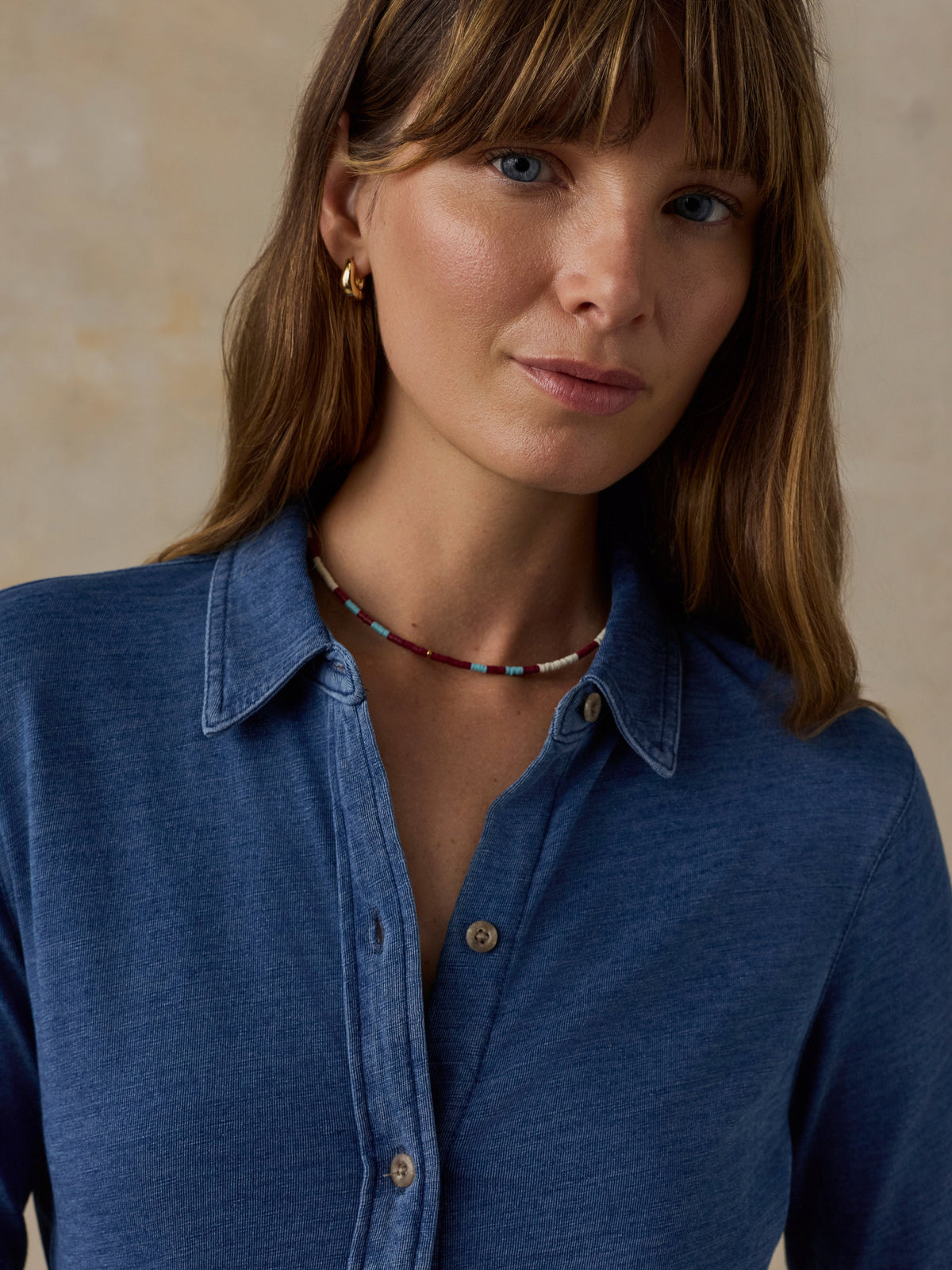 Woman wearing a blue button down shirt against a beige background